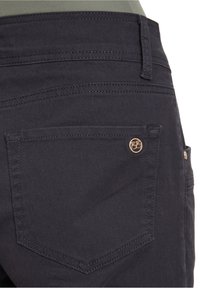 Dark denim pants featuring a back pocket with a gold logo accent, contrasting stitching, and a smooth texture.