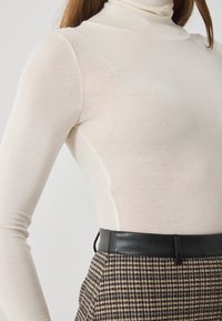 Hosszú ujjú, krém színű garbó felső bordázott textúrával, barna houndstooth mintás nadrággal és fekete bőr övvel párosítva.