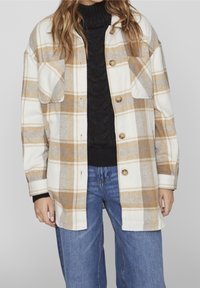 Kostkovaná košile-jacket v béžové, bílé a šedé barvě, se dvěma náprsními kapsami, knoflíky vpředu a volným střihem. Tkanina vypadá měkce a texturovaně.