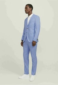 Light blue suit made of fine fabric; tailored jacket with a single button and notch lapels, paired with slim-fit trousers and white sneakers.