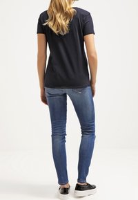 Laivastonsininen t-paita lyhyillä hihoilla, yhdistettynä istuviin sinisiin farkkuihin ja mustiin liukuaviin kenkiin. Malli näkyy selkäpuolelta, hiukset valuavat alas.