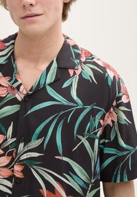 Camicia a maniche corte in tessuto nero con un vivace motivo floreale nei toni del verde, rosa e rosso; chiusura con bottoni, design del collettino tipico.