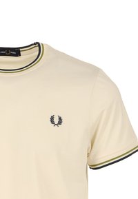 Cremefarbenes Baumwoll-T-Shirt mit rundem Ausschnitt, versehen mit einem grün-schwarz gestreiften Rand und einem dunkel gestickten Logo auf der Brust.