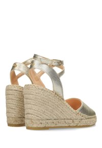 Sandalias de cuña espadrille en dorado metálico con diseño de tiras cruzadas, plataforma de yute texturizado y hebilla ajustable en el tobillo. Forro interior suave.