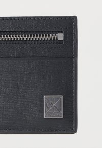 Μαύρο πορτοφόλι από δερματίνη με υφή, με φερμουάρ και ανάγλυφο λογότυπο Calvin Klein. Διαθέτει κομψή ραφή και σύγχρονα σχεδιαστικά στοιχεία.