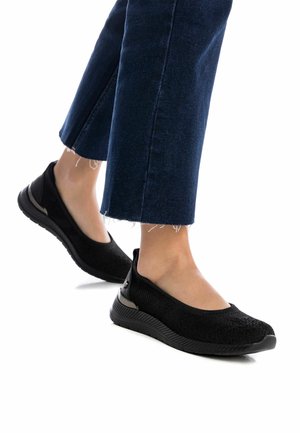Zapatillas negras transpirables tipo slip-on con parte superior de punto texturizado y suela flexible de goma. Presentan un acento sutil en el talón.