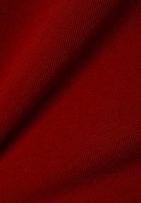 Červená pletenina, texturovaná ribbovým vzorem. Měkký, hladký povrch s mírným leskem, splývá v jemných záhybech.