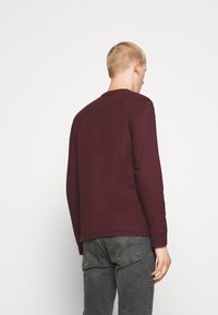 Långärmad skjorta i vinröd, tillverkad av ett texturerat tyg, med rund halsringning och enkel design, kombinerad med grå jeans.