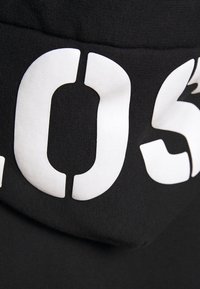 Zwarte stof met grote witte geprinte letters die "LOS" vormen. De textuur lijkt glad met een lichte glans.