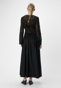 Svart spets topp med lång ärm och mönstrad textur, tillsammans med en svängig svart kjol. Outfitten har eleganta klacksandaler med klossklack.