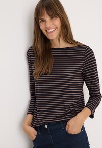 Haut rayé à manches longues bleu marine et beige avec un col rond et un tissu doux et léger. Associé à un pantalon en denim foncé avec des poches latérales.