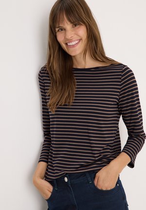 Haut rayé à manches longues bleu marine et beige avec un col rond et un tissu doux et léger. Associé à un pantalon en denim foncé avec des poches latérales.