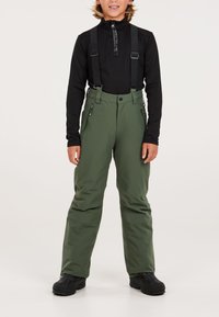 Pantaloni da sci verdi con bretelle nere regolabili, tasche con zip e una finitura liscia, indossati sopra una maglia nera a maniche lunghe.