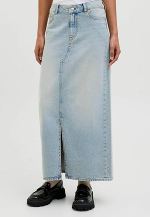 Maxi falda de mezclilla azul clara con una abertura frontal, cinturilla estructurada y diseño de cinco bolsillos. Combinada con zapatos de plataforma negros.