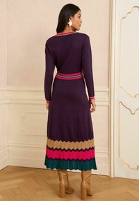 Abito lavorato a maglia a maniche lunghe di colore viola scuro, con una vita scallopata rosa e verde e un orlo multicolore a zigzag.