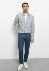 Gestreiftes Hemd zum Drücken, weißer Grund mit marineblauen Streifen, kombiniert mit marineblauen, schmal geschnittenen Hosen und weißen Turnschuhen. Glatter Stoff, lässiges Design.