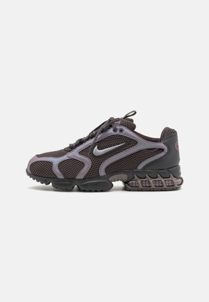Ciemnoszary but do biegania Nike z siateczkową cholewką, srebrnym logo, amortyzowaną podeszwą i sznurowaniem, widziany z boku na białym tle.