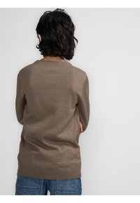 Brauner Strickpullover mit gerippten Bündchen und Saum. Hat eine lockere Passform und eine dezente Textur. Getragen mit blauen, strukturierten Denim-Hosen.