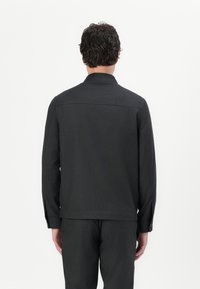 Black, long-sleeve shirt with a collar, made from a smooth fabric. Features a straight cut and buttoned cuffs. Back view shown.