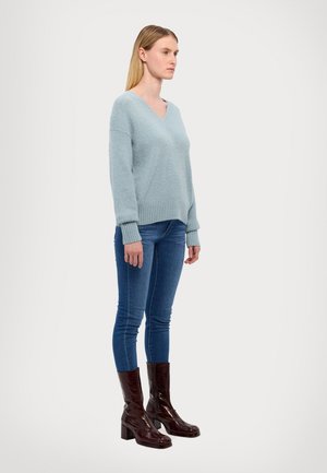 Lys blå, teksturert genser med V-hals og ribbestrikket kant, kombinert med tettsittende denimjeans og glinsende, burgunder knelange høyhælte støvler.