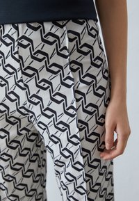 Un pantalon à motifs noir et blanc arbore un design ondulé sur un tissu lisse, avec des plis et une coupe décontractée.
