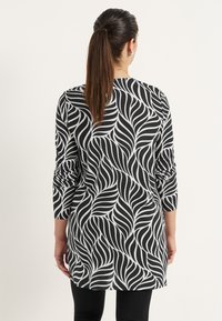 Zwart-witte tuniek met een bladpatroon, lange mouwen en een losse pasvorm, gemaakt van een gladde, elastische stof.