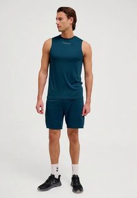 Sportski gornji dio bez rukava u tirkiznoj boji i pripadajuće kratke hlače od glatkog materijala, no šeni s crnim tenisicama i bijelim čarapama s crnim detaljima.