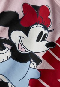 Souris de cartoon souriante avec un grand nœud rouge, des oreilles noires, des gants blancs et une jupe bleu clair sur fond de tissu rose avec du texte rouge.