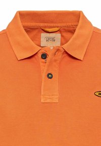 Oranje poloshirt van gestructureerde stof, met een kraag, een placket met twee knoppen en een geborduurd logo in het zwart aan de linkerzijde.