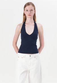 Marineblauwe haltertop in een aansluitend ontwerp, met een diepe V-hals. Draagt een combinatie met witte wijde jeans, wat een contrast in kleur en stijl creëert.