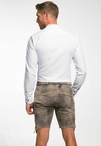 Weißes Langarmhemd mit Knopfmanschetten, kombiniert mit beigen Leder-Shorts mit dekorativen Nähten und seitlichen Schnürungen.