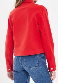 Veste en jean rouge avec un col à revers, des poignets boutonnés et un ourlet court. Portée avec un jean bleu taille haute. Texture lisse.