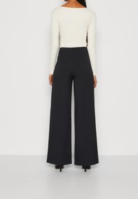 Pantaloni neri a gamba larga realizzati in un tessuto morbido, abbinati a un top attillato a maniche lunghe color crema con un ampio scollo.