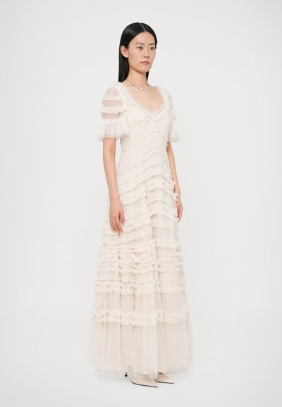 Μακρύ κρεμ φόρεμα με υφή βολάν και φούστα πολλαπλών στρωμάτων από τούλι. Διαθέτει κοντά φουσκωτά μανίκια και V-λαιμόκοψη, διακοσμημένο με πουά σχέδια.