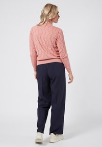 Jasnoróżowy sweter z teksturowanym wzorem falistym, z prążkowanymi mankietami i dołem. Połączony z ciemnogranatowymi spodniami w szerokim kroju i jasnymi sneakrsami.