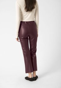 Pantaloni din piele eco burgundy cu un design ajustat, lungime scurtă și o textură elegantă. Asortați cu pantofi negri slip-on.