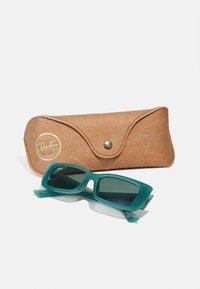 Ochelari de soare din plastic teal cu rame dreptunghiulare, însoțiți de un etui din piele sintetică maro deschis, cu un logo auriu și închidere cu capsa.