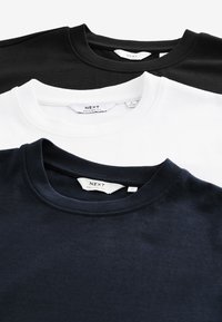 Tre T-shirts i sort, hvid og marineblå med rund halsudskæring, blød bomuldsagtig tekstur og synlige mærkater indeni kraverne.