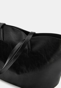 Borsa a spalla in ecopelle nera con texture liscia, parte superiore curva e doppi manici. Design semplice senza hardware visibile o decorazioni.