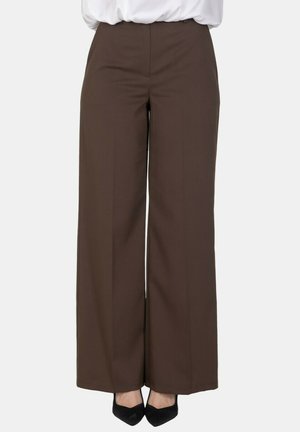 Pantaloni marroni a gamba larga indossati con décolleté nere a punta e una camicetta bianca infilata, mostrati dalla vita ai piedi.