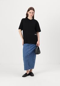 Svart kortermet t-skjorte med løs passform, kombinert med et langt denimskjørt.Outfitet fullføres med svarte flate sko og en liten håndveske.