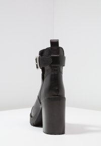 Czarne botki na wysokim obcasie, wykonane z teksturowanej skóry, z zapięciem na klamrę oraz solidnym blokowym obcasem, z okrągłym noskiem i pętelką z tyłu.