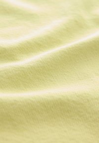 Tessuto di colore giallo chiaro, con trama morbida e leggermente elasticizzata, che mostra lievi ondulazioni e sfumature sottili sulla superficie.