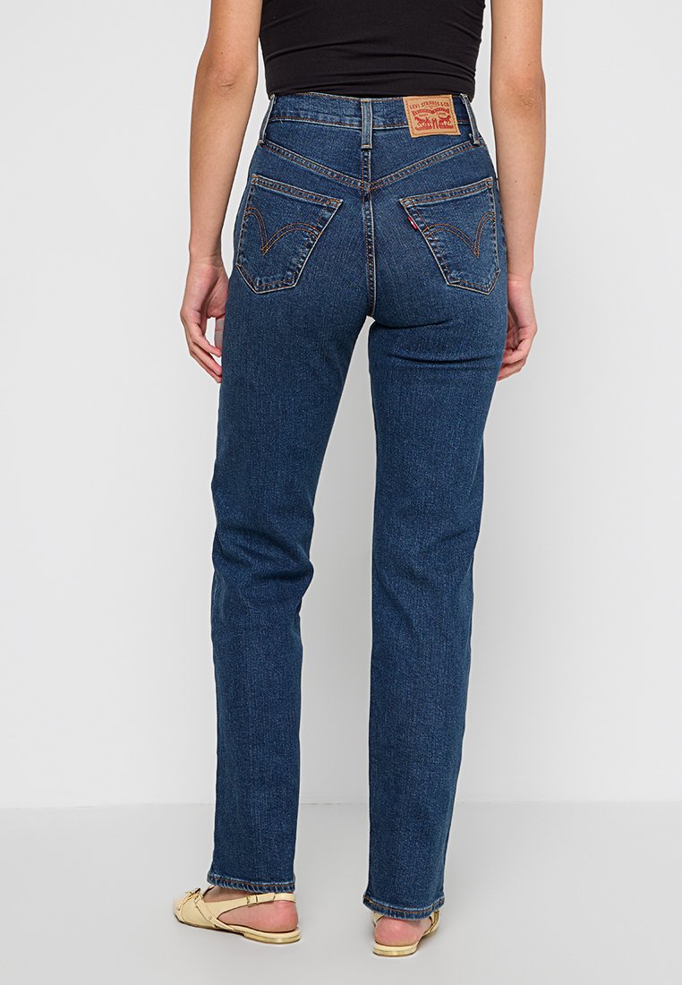 Jeans in denim blu con gambe dritte, vita alta e due tasche applicate sul retro. Presentano un'etichetta in pelle beige sulla vita.