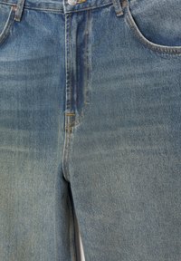 Jean en denim bleu vue de face montrant la fermeture éclair, le bouton, les passants pour ceinture et les poches avant avec des détails de couture orange visibles.