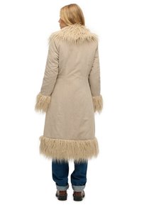 Manteau beige en velours côtelé avec col et poignets en fausse fourrure, présentant une coupe mi-longue avec une bordure duveteuse à l'ourlet et aux manches.