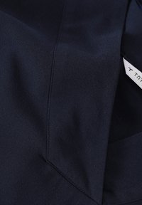 Tela azul marino con una textura suave, que presenta costuras limpias y anguladas y una etiqueta en el borde. Presente un ligero brillo.