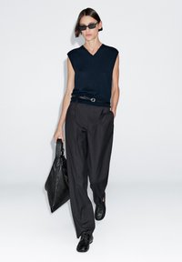 Námořnická v-neck bezrukávová halenka, přizpůsobené černé kalhoty, černá kožená taška a černé boty. Jednoduchý design s minimálními akcenty.