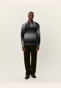 Pulover tricotat ombre gri cu guler cu nasturi, asortat cu pantaloni din catifea verde închis. Modelul stă pe un fundal neutru.