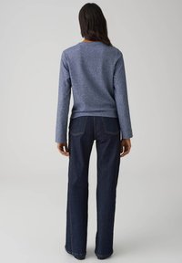 Blauw gemêleerd shirt met lange mouwen gecombineerd met een high-waisted donker denim jeans, voorzien van een rechte pijp en contrasterende stiksel details.
